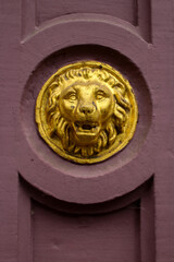 closeup of a lions head golden relief, on an old red colored stone building 