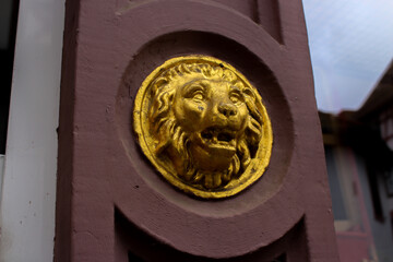 closeup of a lions head golden relief, on an old red colored stone building 