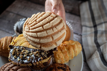 Manipulacion de alimentos, manejo de comida en la cocina, mano agarrando pan dulce mexicano de nombre CONCHA, con un plato de panes dulces al fondo con una servilleta de tela al lado, vista aerea
