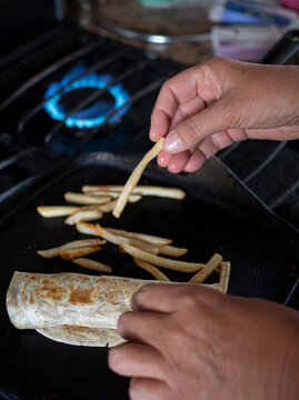 Manipulacion de alimentos, manejop de comida en la cocina, mano agarrando una papa frita de un comal con una quesadilla al lado y el fuego de la estufa por un lado, en una cocina oscura