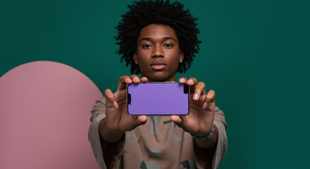 Stylish young man presenting a vibrant purple smartphone, showcasing technology and modern lifestyle on an attractive teal and pink background