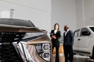 Automotive sales professionals discussing vehicle features in a modern showroom, with a focus on the sleek design of a brown SUV and a white truck in the background