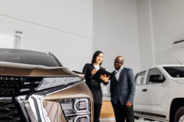 A male auto consultant and a female customer discuss a car's specifications in a well-lit showroom, demonstrating a high level of customer service and professionalism.