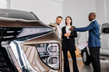 Close-up of modern vehicle front showcasing sleek design, while diverse individuals engage in...