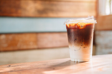 Iced coffee concept. Refreshing iced coffee drink in a clear cup with layered colors against a rustic wooden background in warm sunlight