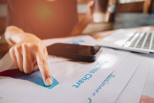 Business analysis concept. Person Pointing at Business Chart while Holding Coffee Cup in Modern Workspace with Laptop and Smartphone
