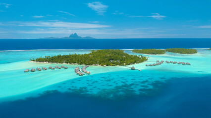 Fototapeta premium Luxury resort photos of Bora Bora tropical paradise islands with palm trees, thatched bungalows. Aerial perspective photography, coral reef, azure ocean, sky with clouds on horizon. French Polynesia
