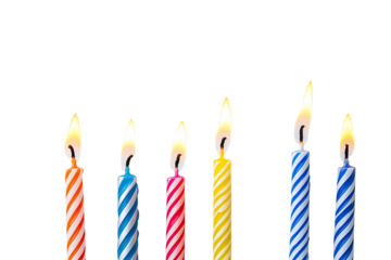 Seven lit birthday candles against stark black backdrop, varying colors/heights