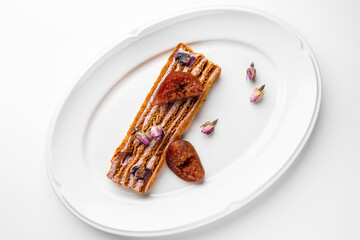 Elegant gourmet dessert plated on a white dish, featuring layered pastry topped with figs, dried rosebuds, and powdered sugar. Fine dining presentation, minimalistic and artistic.