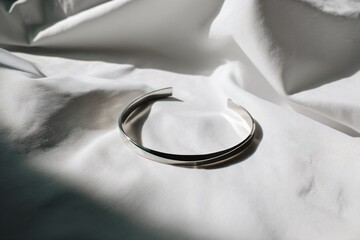 A sleek silver cuff bracelet rests on draped white fabric, illuminated by soft natural light.