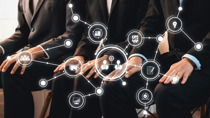 A group of business professionals is sitting together, surrounded by digital icons representing...