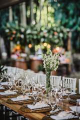 Elegant outdoor wedding reception table with a tall floral centerpiece and beautiful bokeh background.