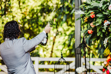 Groom celebrating by popping a bottle of champagne at an outdoor wedding reception