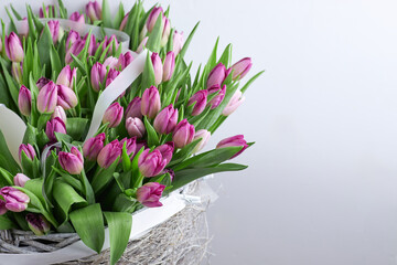 Abundant bouquet of pink and purple tulips in rustic wicker basket with translucent ribbon on green metal stand
