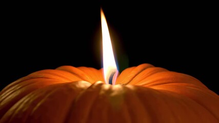 Close-up of pumpkin candle flame burning steadily in dark background showing light and texture on pumpkin - Powered by Adobe