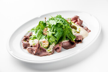 Gourmet roast beef salad with arugula, spinach, capers, and creamy dressing on a white plate. Minimalist presentation, fresh ingredients, restaurant-style plating.