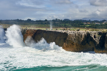 Visitors and tourists walk above the cliffs of Pria with waves crashing against the rocks