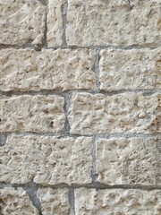 Close-up and detail of a dry-stone wall (or wall with exposed concrete joints) made of limestone blocks. The texture is extremely rough, porous, and textured, in off-white/light beige tones.