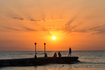Paralia, Katerini, Greece, 14.08.2025: Sunrise over the sea in Paralia, Katerini, Greece. Silhouettes of people and a girl standing against the sun.