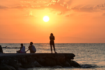Paralia, Katerini, Greece, 14.08.2025: Sunrise over the sea in Paralia, Katerini, Greece. Silhouettes of people and a girl standing against the sun.