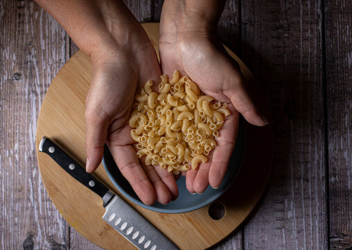 Manipulacion de alimentos, manejo de comida en la cocina, manos de mujer hispana mexicana agarrando pasta de coditos sin cocinar ,cruda, vista cenital