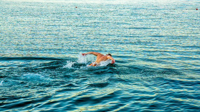Man swimming butterfly stroke in open sea water creating splashes under natural daylight during summer workout or training session