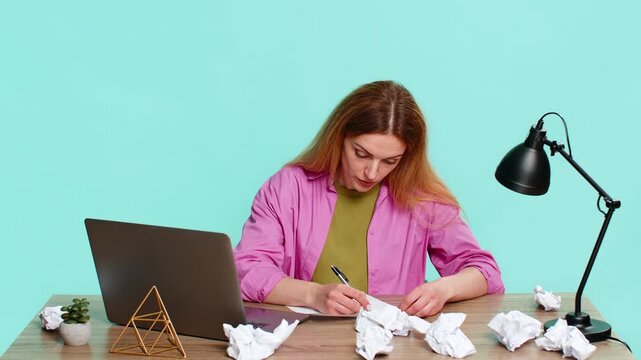 Middle-aged woman sits at table with laptop, crumples sheet of paper in hands showing disappointment, frustration from error in report. Girl isolated on blue background shows stress and second attempt