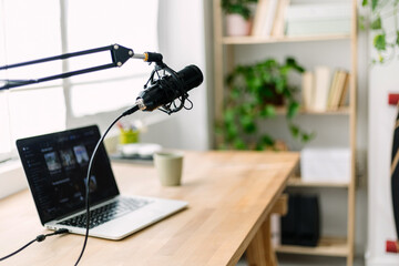 Modern podcast recording setup with microphone and laptop on desk in home studio. Creative workspace for digital media production and online broadcasting concept.