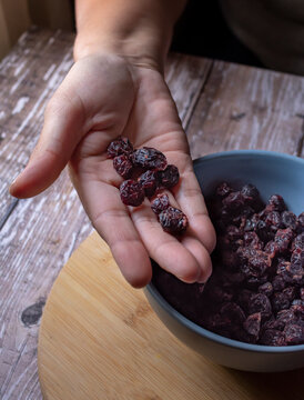 Manipulacion de alimentos, manejo de comida en la cocina, mano femenina tomando pasas o pasitas de un tazon azul sobre una mesa de madera