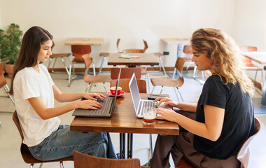 Two young women working on laptops in a bright cafe