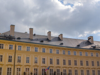 Obraz premium Classical yellow facade of a large historical palace building with numerous windows and decorative chimneys against a soft cloudy autumn sky.