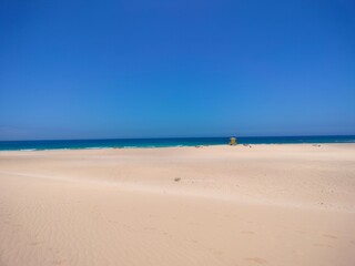 Golden sand dunes of Fuerteventura in warm sunlight. Desert landscape with soft sand lines and a clear blue sky. The natural beauty of the Canary Islands, perfect for travel or nature themes.