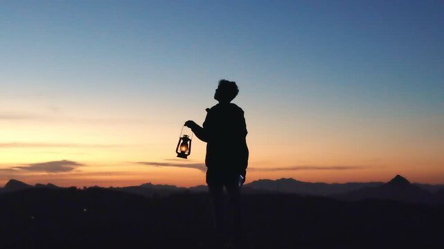 Silhouette of a man holding a lantern at sunset, symbolizing faith, inner light, and spiritual reflection in a peaceful landscape