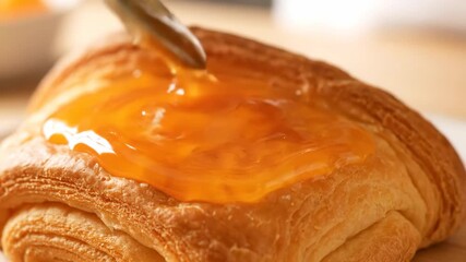 Spoon pouring sweet orange jam or marmalade onto a golden brown croissant delicious flaky breakfast pastry footage - Powered by Adobe