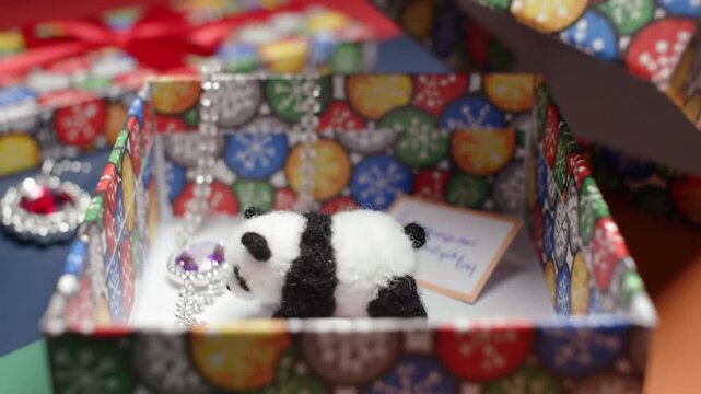 A small panda pendant necklace rests inside a colorful gift box, accompanied by a handwritten note.  The box is decorated with a festive pattern, hinting at a celebratory occasion