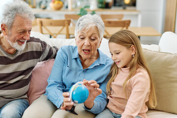 Portrait of grandparents and granddaughter having fun together exploring globe teaching and learning at home