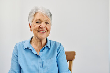 Portrait of a happy senior elderly woman standing by window and relaxing at home