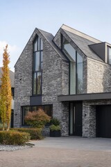Obraz premium Modern stone house with large windows in a suburban neighborhood on a clear day, showcasing sleek design and stylish architecture