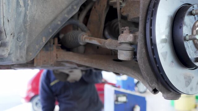 Mechanic performing car suspension diagnostics on a vehicle lifted on a hydraulic hoist