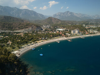 Aerial drone photo of coastal town with sandy beach, blue sea and mountains. Scenic summer travel destination and seaside landscape. Camyuva, The Gulf of Antalya, Turkey