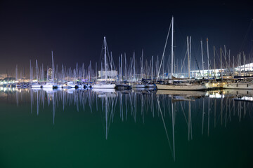 Stunning night scene of sailboats docked in harbor reflecting in calm water under dark sky creates peaceful feeling perfect for travel and vacation ads