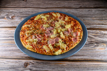 Warm pizza featuring ham and pineapple sits on a blue plate. The wooden table background adds a rustic touch. Ideal for casual dining or sharing with friends