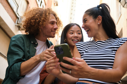 Group of young tourists using smartphone and laughing in the street