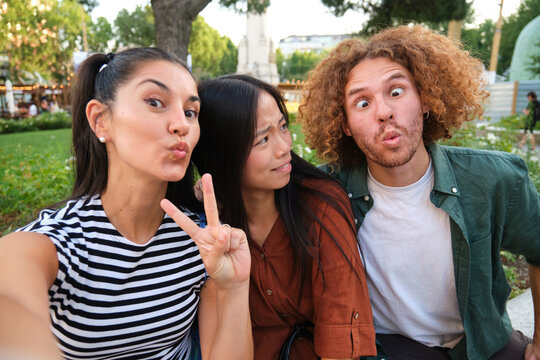 Three friends are making funny faces and taking a selfie in a park, enjoying their time together