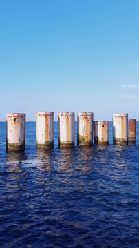 Seaside landscape of Baltic sea coast with calm waves rolling on metal piles row forming shore protection dam construction under clear blue sky at summer day. Vertical seascape natural background.