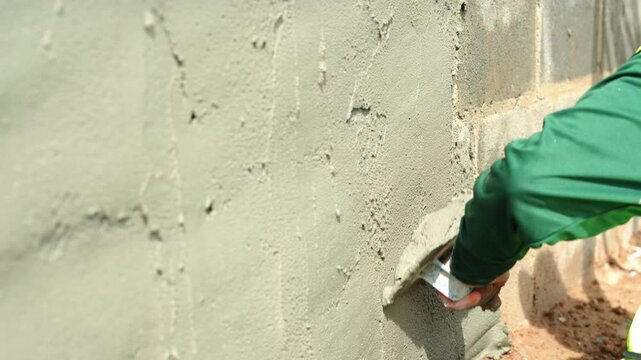 A plasterer is plastering cement on a cement surface.