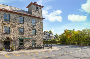 Exterior daytime view of century-old three storey limestone building with tower, paned windows and doors, old house in background, nobody