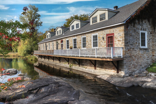 An old stone mill building converted to residential row units units alongside calm water on sunny day, nobody