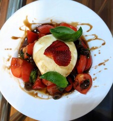 Fresh salad with burrata, tomatoes, and basil on a white plate