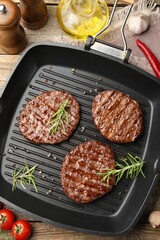 Pan with grilled patties, tomatoes and spices on wooden table, flat lay